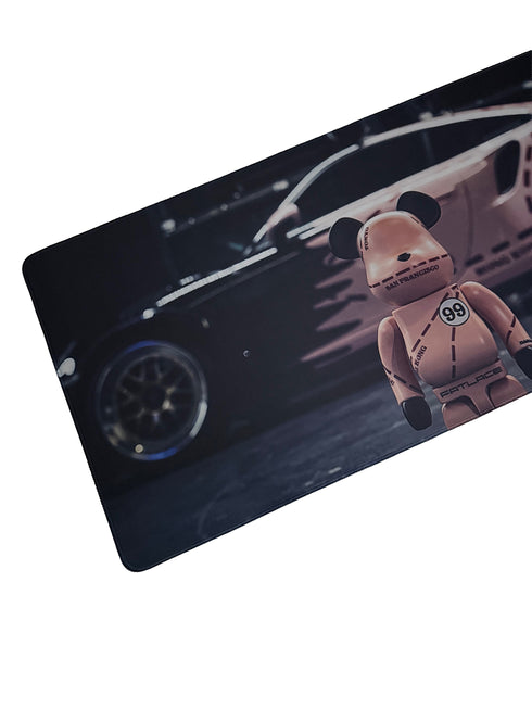 Gaming muismat met roze raceauto en cartoonbeer in race-outfit – 900x400mm bureaumat